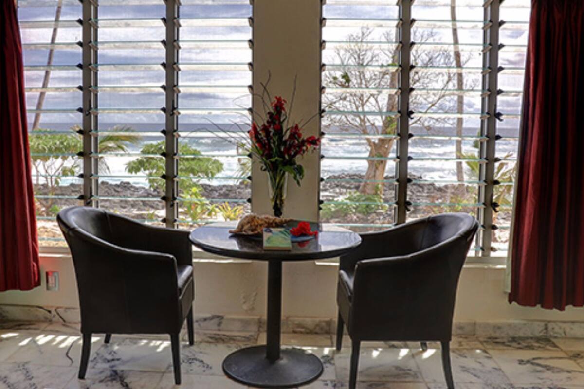 Ein Zimmer mit einem großen Fenster, zwei Stühlen, einem kleinen Tisch und einer Vase mit Blumen.