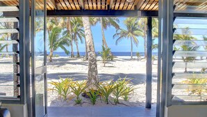 Vista de la playa a través de una puerta de cristal, con palmeras y arena.