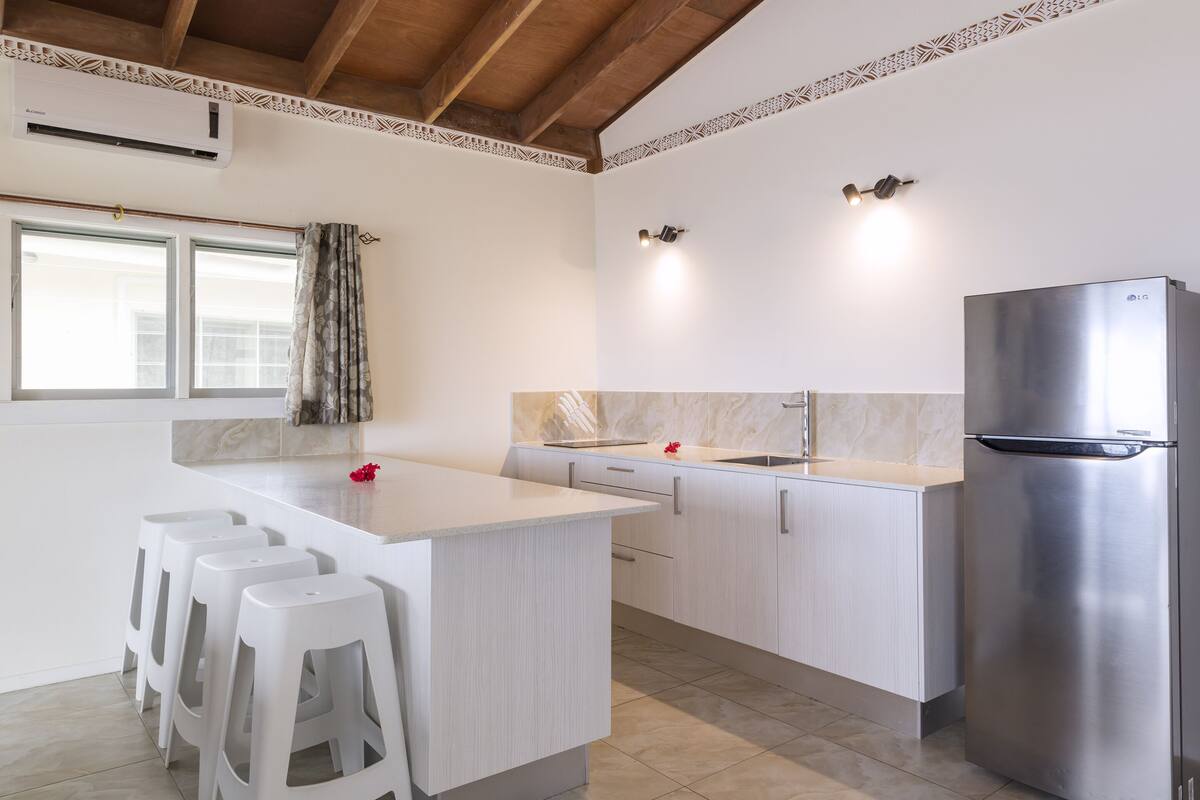 Eine moderne Küche mit weißen Schränken, einem Edelstahlkühlschrank und einer Bar mit Hockern.