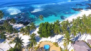 Un complejo turístico en la playa con piscina, palmeras y vistas al océano.