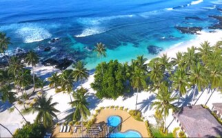 Un complexe hôtelier de bord de mer doté d’une piscine, de palmiers et offrant une vue sur l’océan.