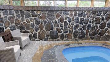 Un área de piscina interior con paredes de piedra y suelo de baldosas, rodeada de sillones de mimbre.
