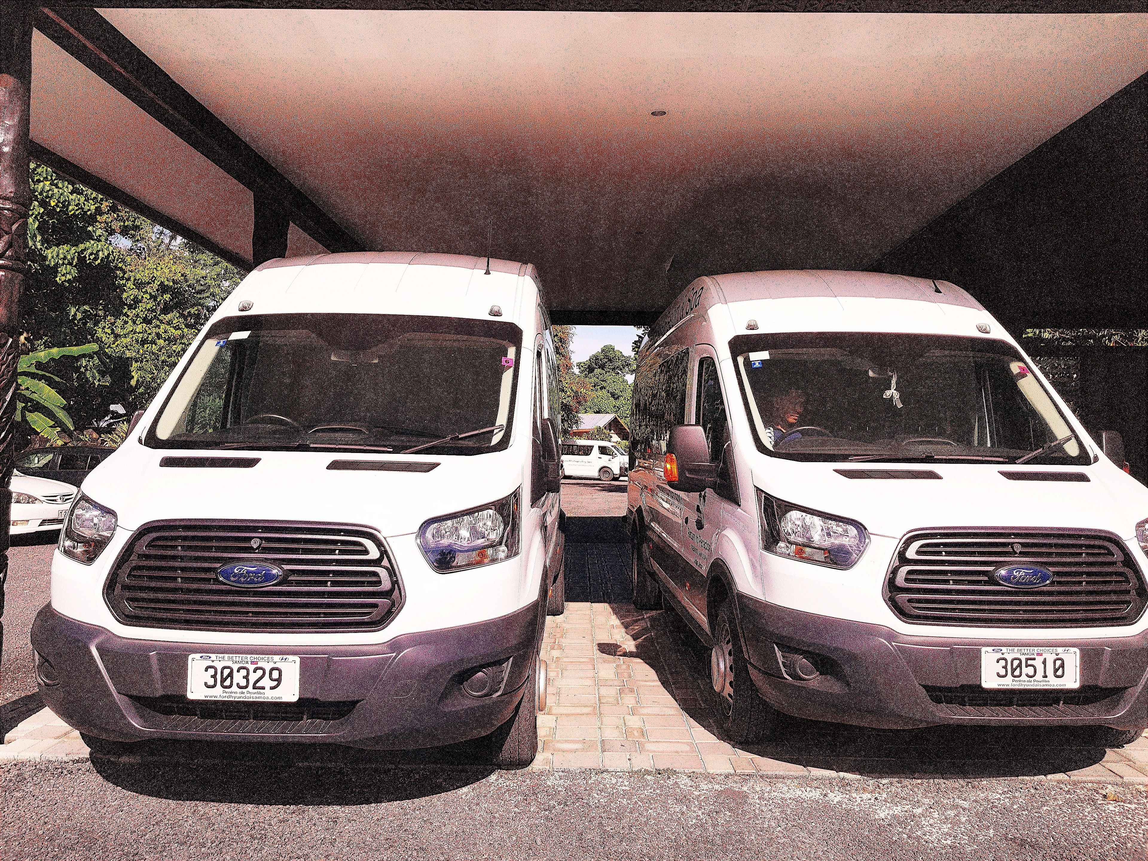 Two white vans parked under a covered area with a brick pavement.