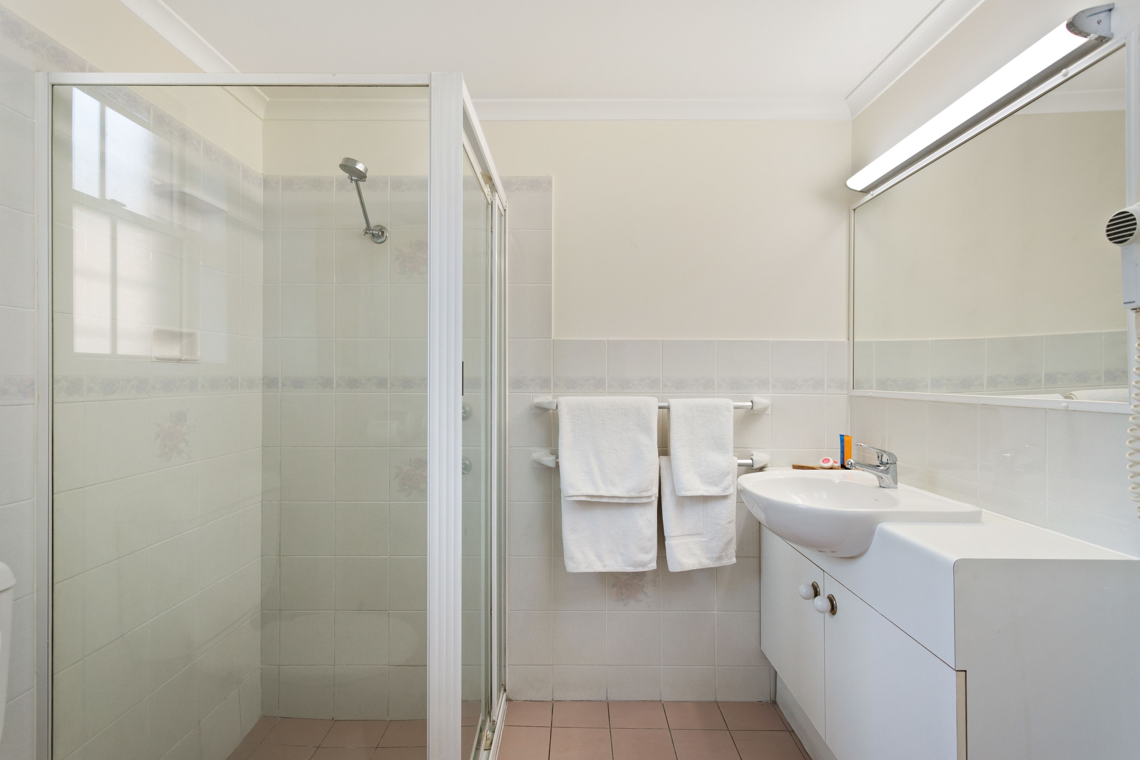 Een moderne badkamer met een douchecabine van glas, een wit wastafeltje en een spiegel erboven.