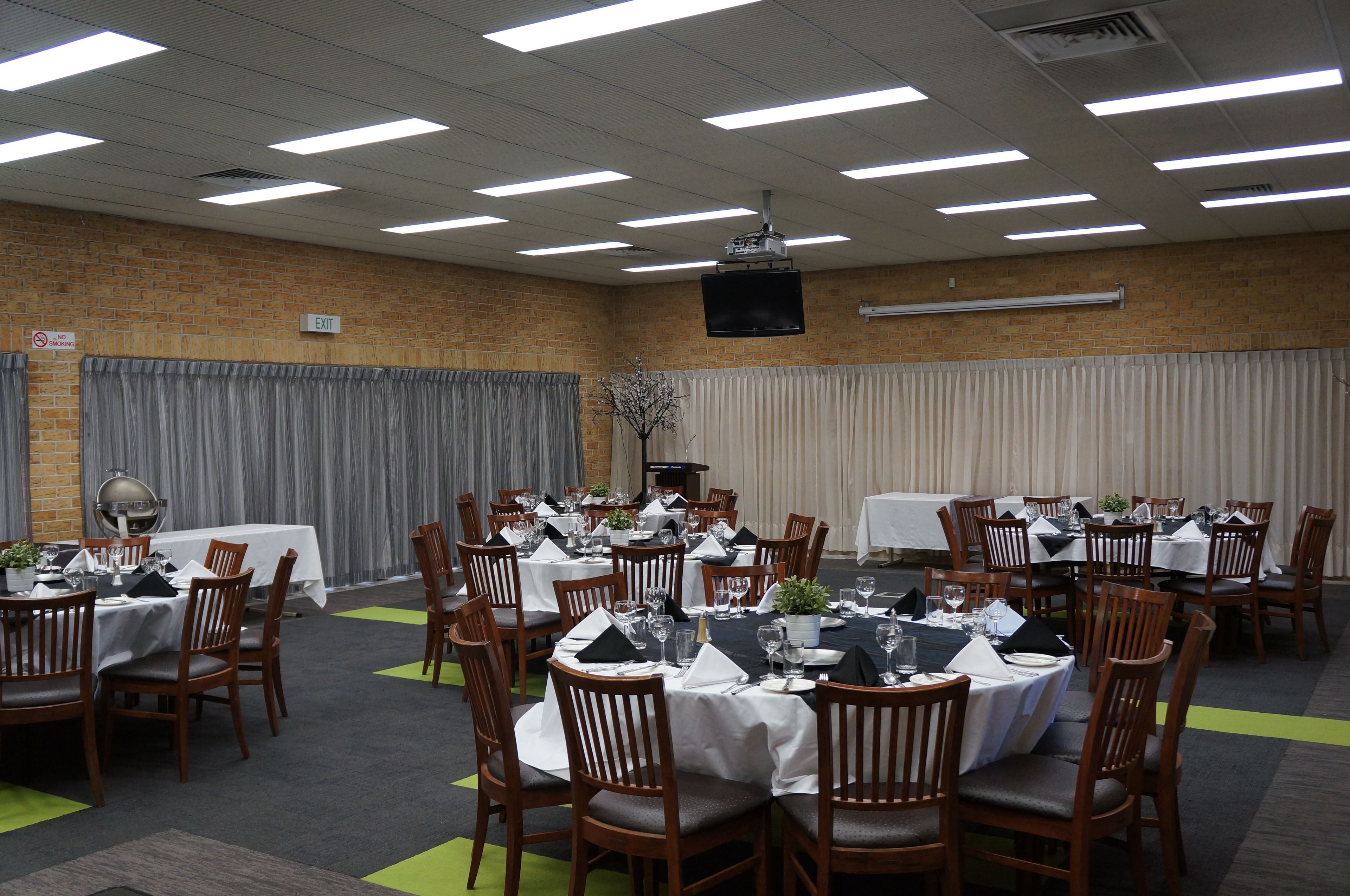 A conference room with multiple tables set for dining, equipped with chairs, tables, and a projector.