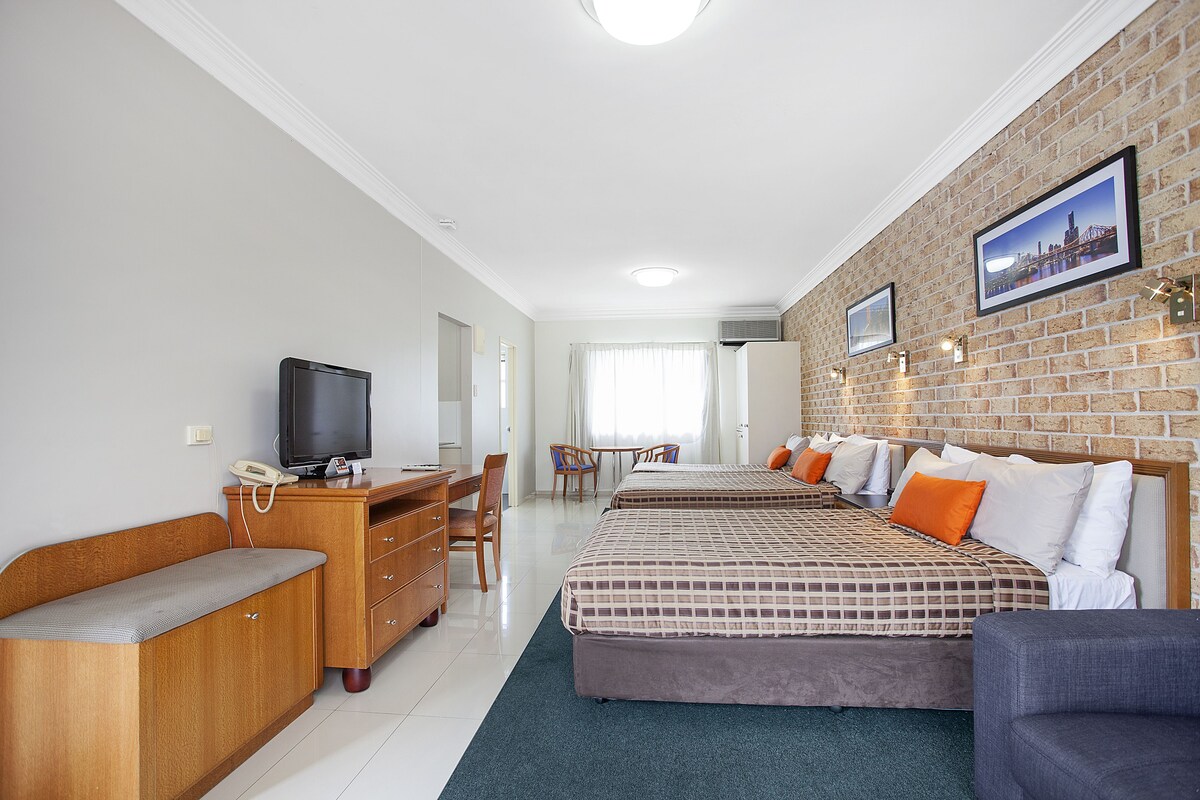 A hotel room with a desk, two beds, a television, and a brick wall.