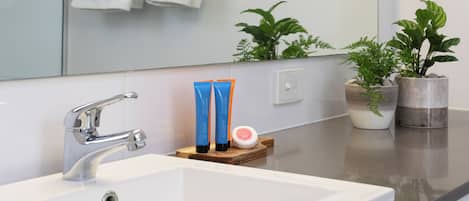 A bathroom with a white sink, a mirror, a towel rack with folded towels, and two potted plants on the counter.