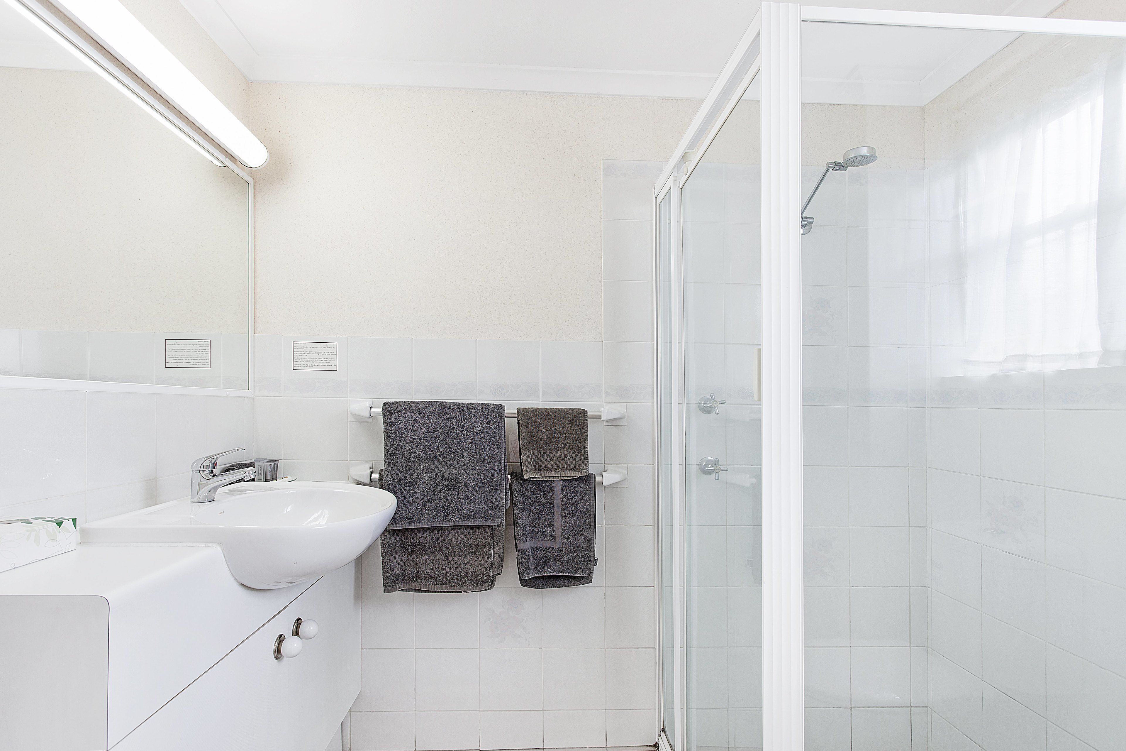 A modern bathroom with a white sink, a glass shower enclosure, and two towels hanging on a rack.