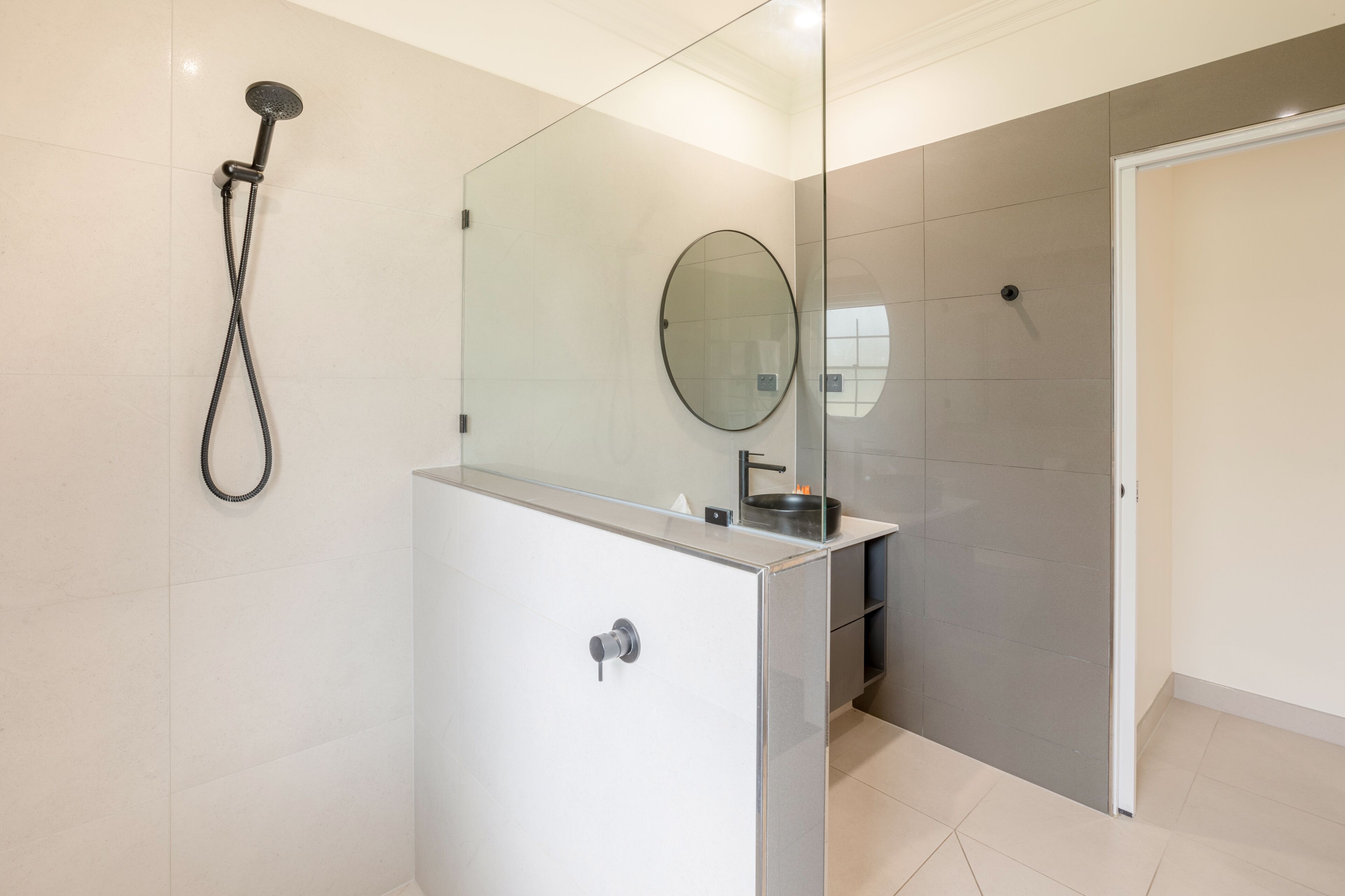 A modern bathroom with a glass shower enclosure, a round mirror, and a white vanity.