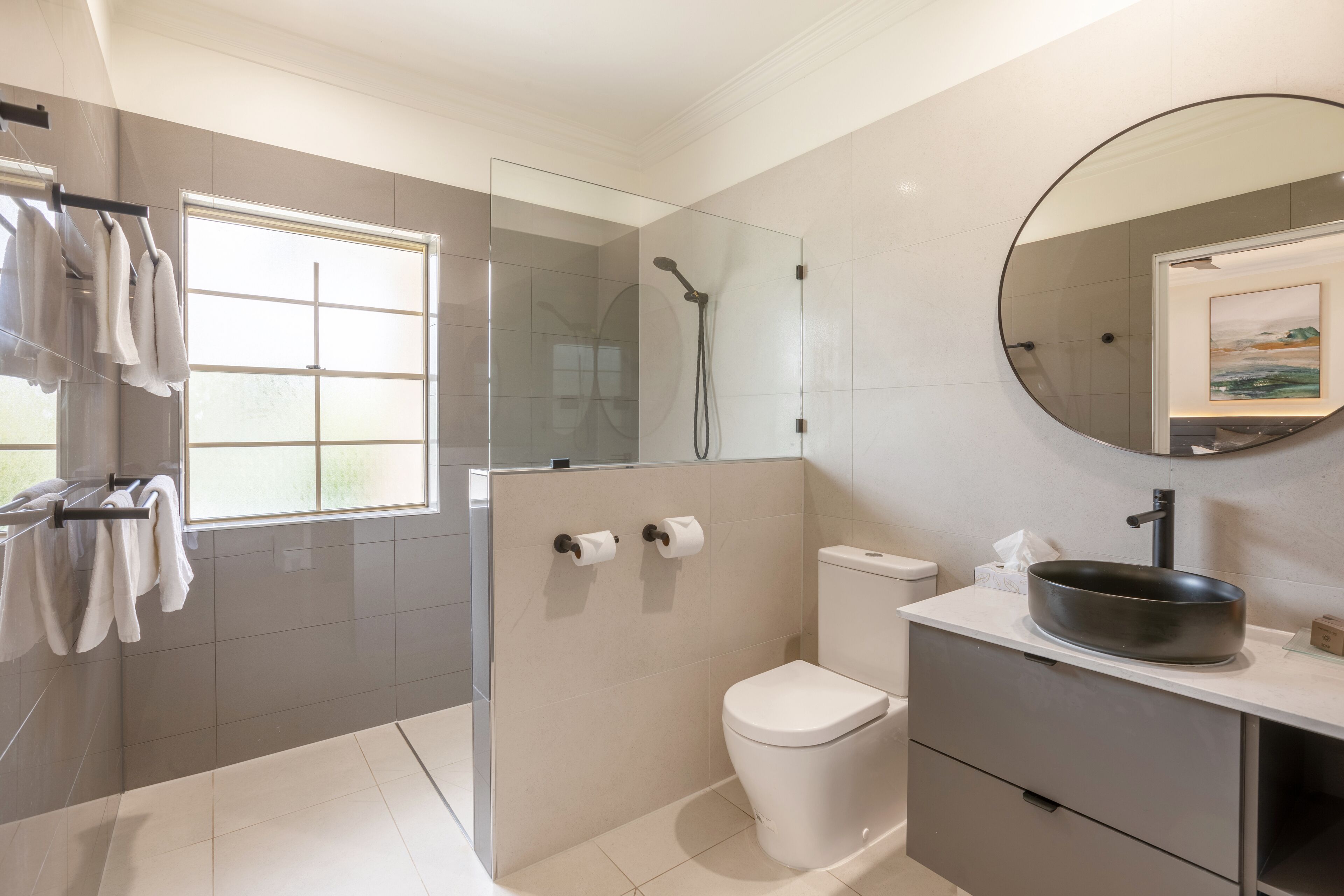 A modern bathroom with a glass-enclosed shower, a toilet, and a vanity with a sink and mirror.