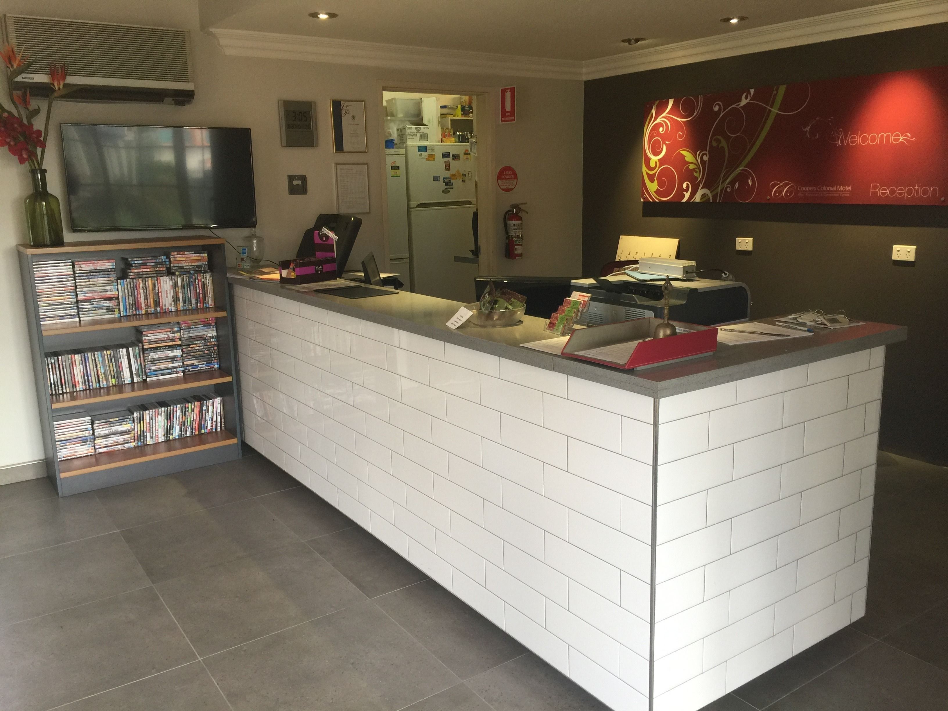 A reception area with a tiled counter, a television, a bookshelf with DVDs, and a decorative wall piece.