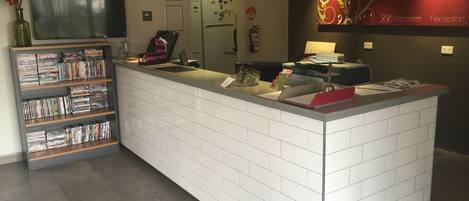 A reception area with a tiled counter, a television, a bookshelf with DVDs, and a decorative wall piece.