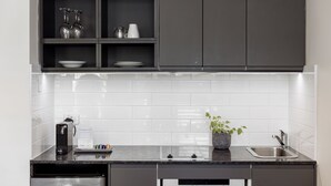A modern kitchen with dark cabinets, white tiles, a built-in dishwasher, and a sink. - Coopers Colonial Motel (Acacia Ridge)
