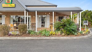 A restaurant with a brick facade, large windows, and a covered outdoor seating area with plants. - Coopers Colonial Motel (Acacia Ridge)