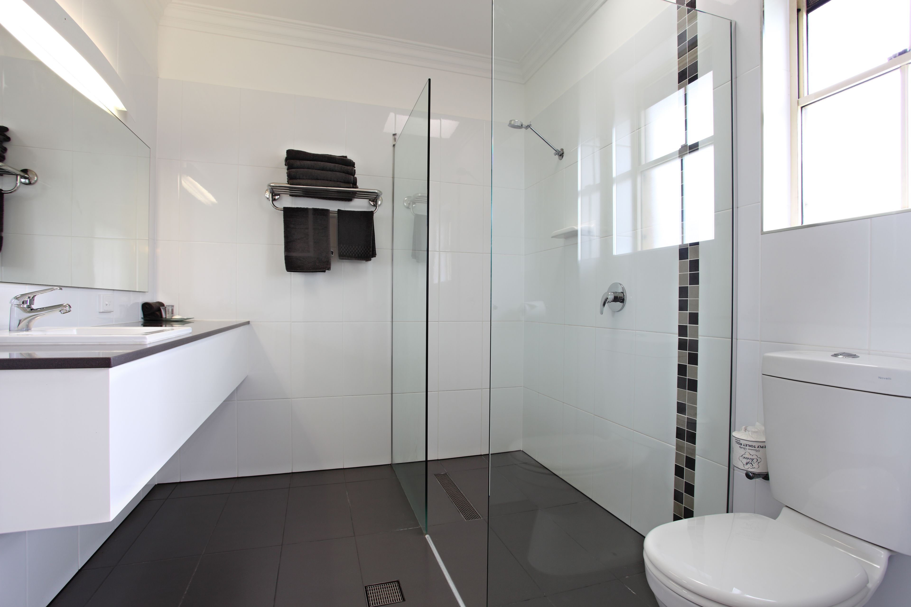 Un baño moderno con cabina de ducha de vidrio, azulejos blancos, un lavamanos blanco y un inodoro.