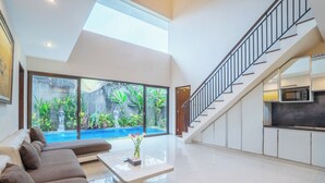 Amplia sala de estar con un gran ventanal con vistas a una piscina, un conjunto de sofás y una escalera que lleva a un nivel superior.