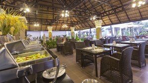 Un espacio de comedor al aire libre con mobiliario de mimbre, estaciones de buffet y techo de paja.