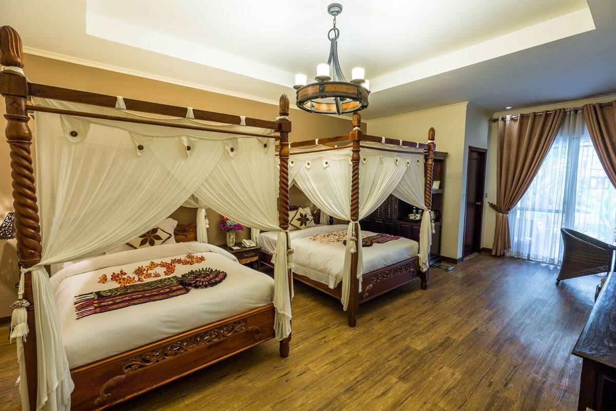 A four-poster bed with white drapes, a chandelier, and a wooden floor in a hotel room.