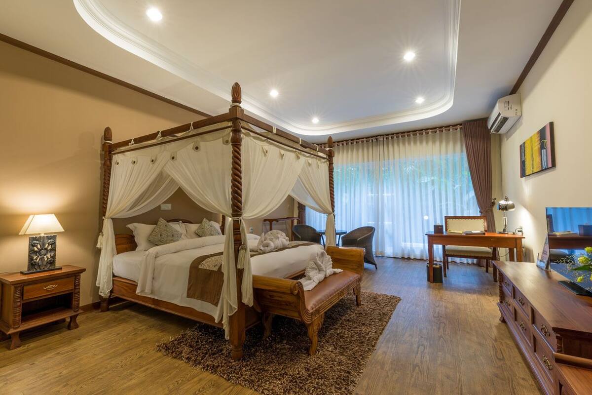 A four-poster bed with a canopy, a desk with a chair, a television, and a large window with curtains.