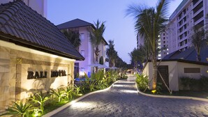 Entrada de hotel con un camino adoquinado, palmeras y un letrero que dice "BALI HOTEL".