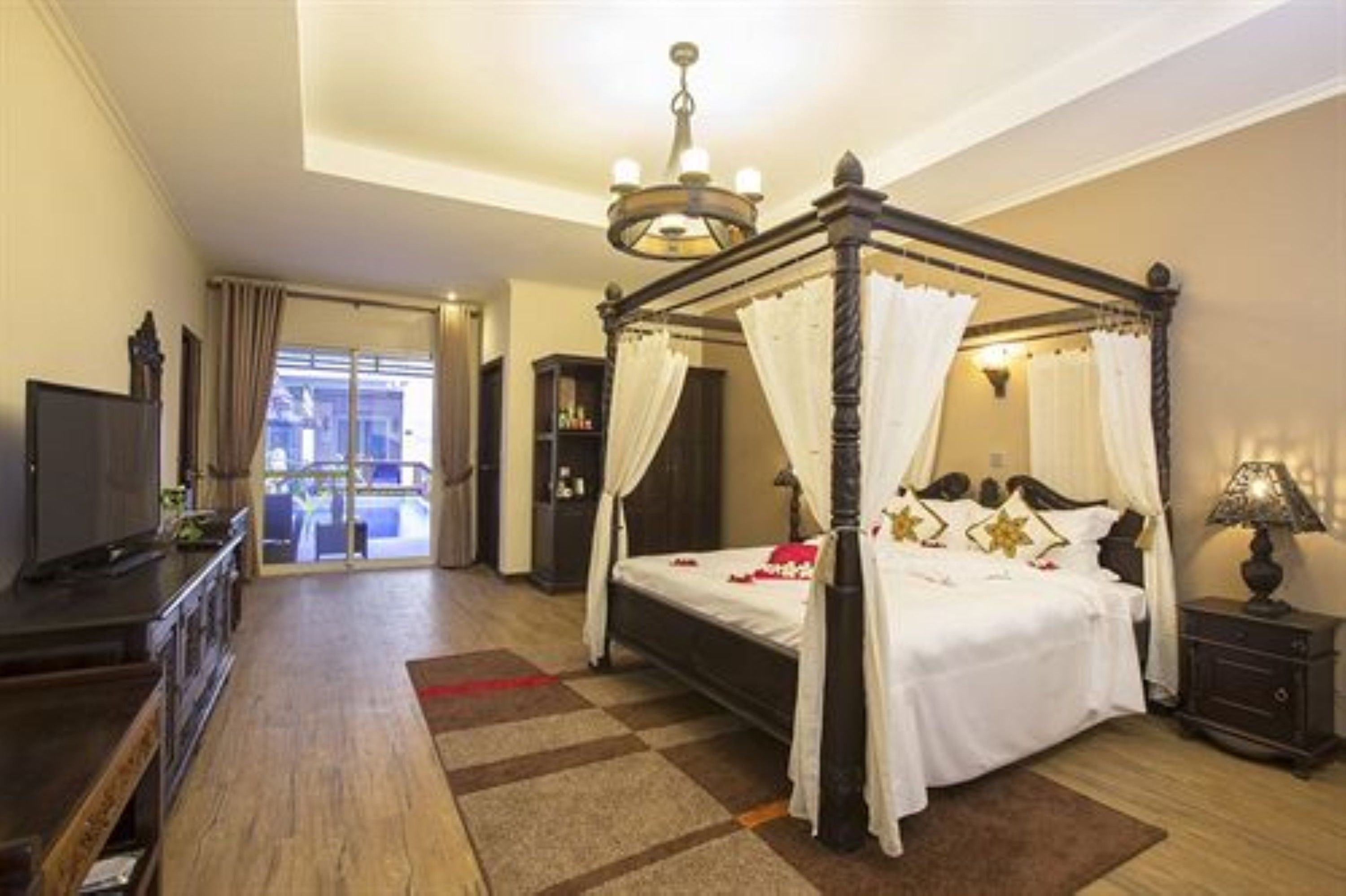 A four-poster bed with a canopy, a television on a dresser, and a nightstand with a lamp.