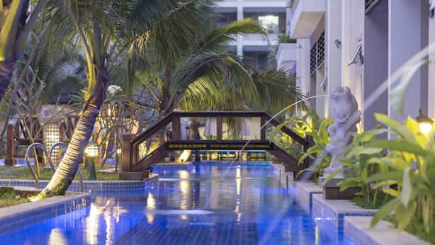 Una piscina con un puente de madera, palmeras y una estatua.