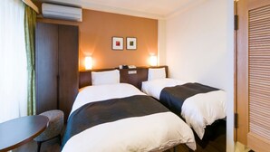 Ett hotellrum med två sängar, ett litet bord, en stol och en luftkonditioneringsanläggning.