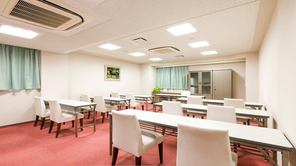 A conference room with tables and chairs, a large window with curtains, a refrigerator, and a ceiling vent. - APA Hotel Fuji Chuo (Fuji)
