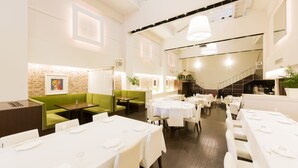 En restaurang med vita bord, gröna sittplatser och en vägg av tegelsten.