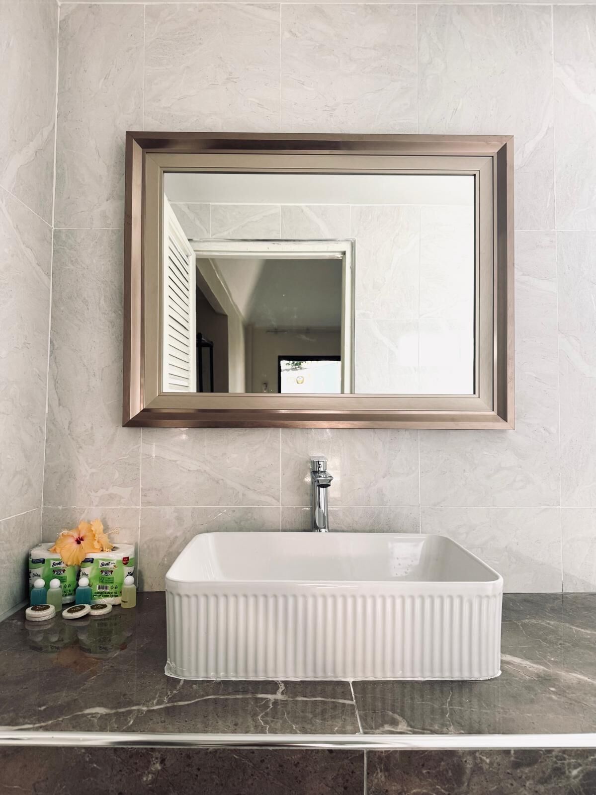 A bathroom with a rectangular sink, a mirror with a wooden frame, and a toilet paper dispenser on the counter.