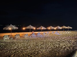 Una playa con filas de tumbonas y sombrillas de paja, evocando un ambiente de resort.