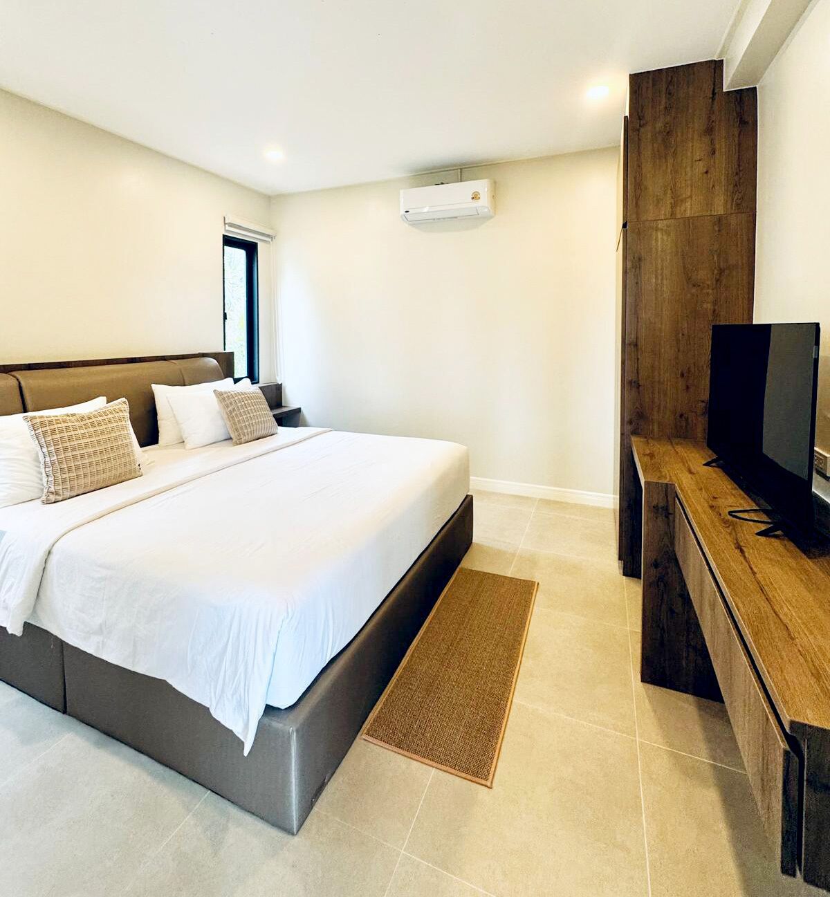 Un dormitorio moderno con una cama grande, un mueble de televisión de madera y un aire acondicionado de pared.