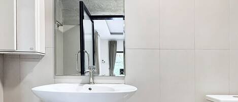 Un baño con un lavamanos blanco, un espejo, una cesta de mimbre y un cubo de basura.