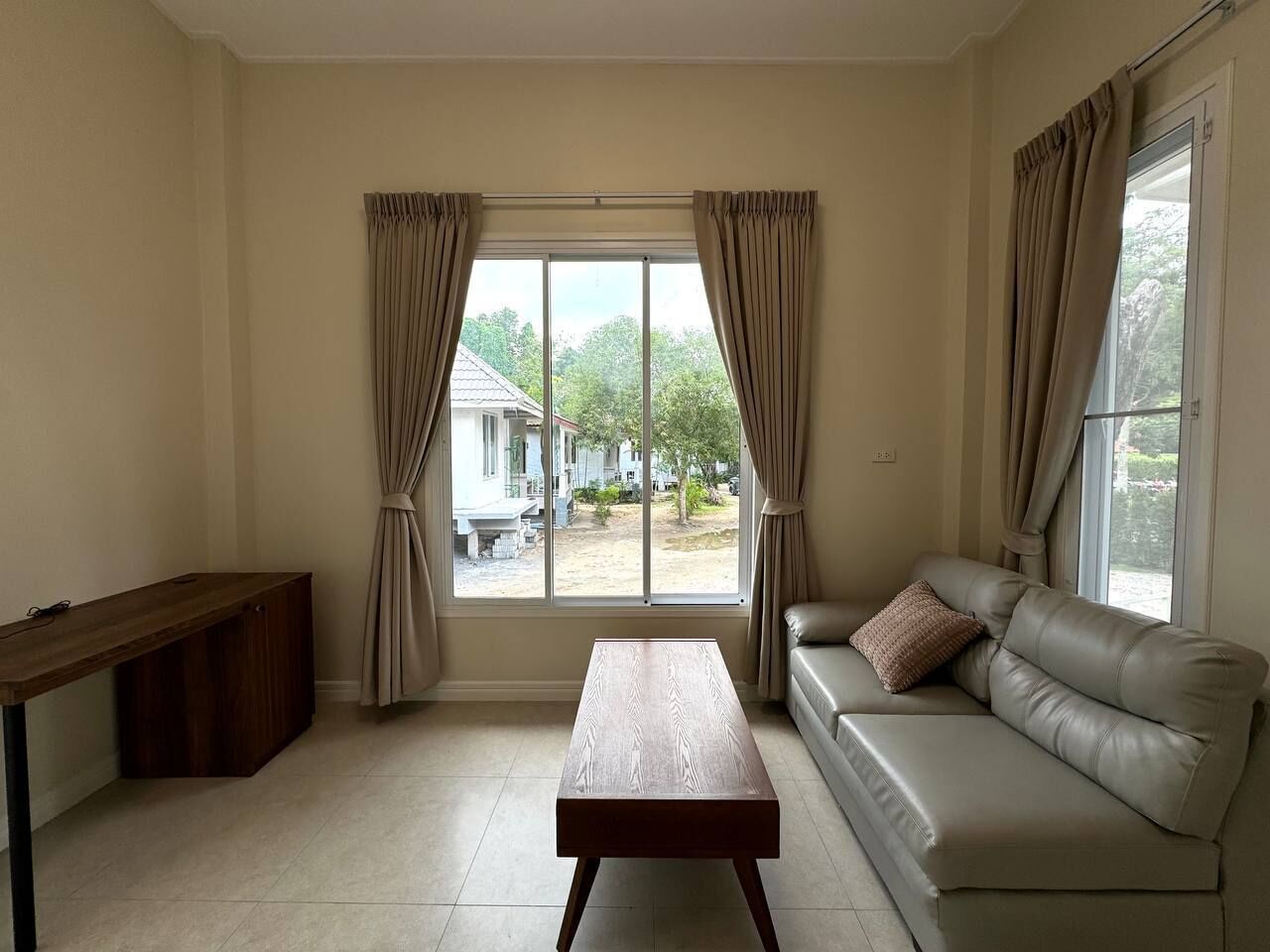 Una sala de estar con sofá, una mesa de centro de madera y un ventanal con cortinas.