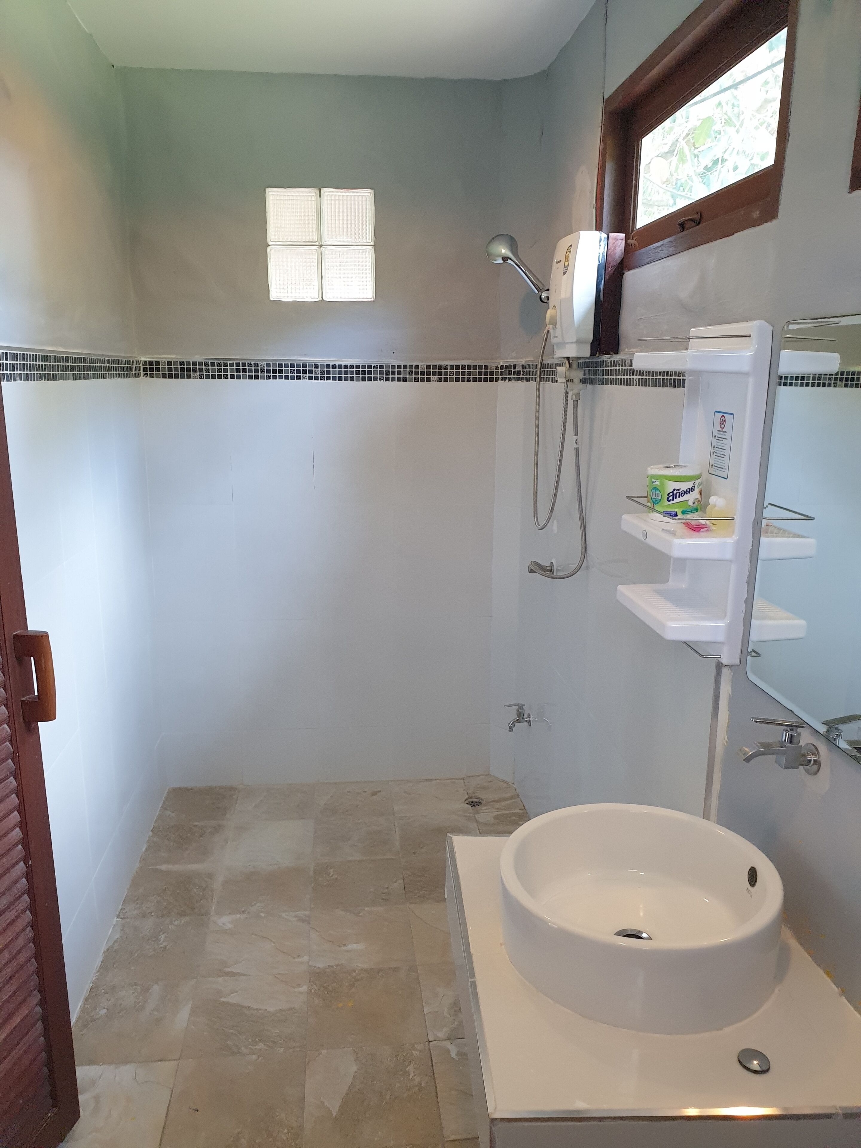 A bathroom with a white sink, a shower, and a small window.