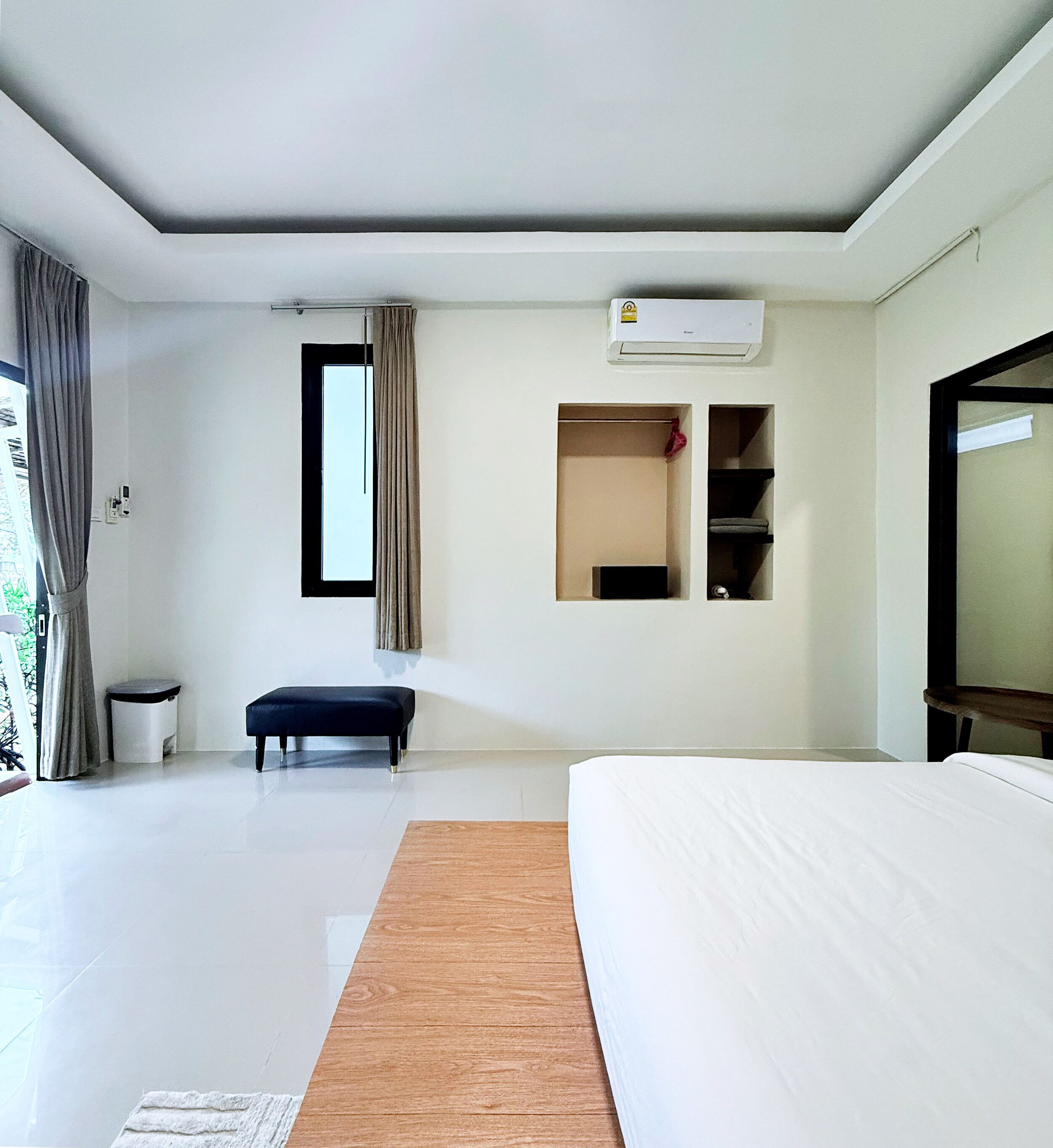 A modern hotel room with a large bed, a small bench, a wardrobe, and a window with curtains.