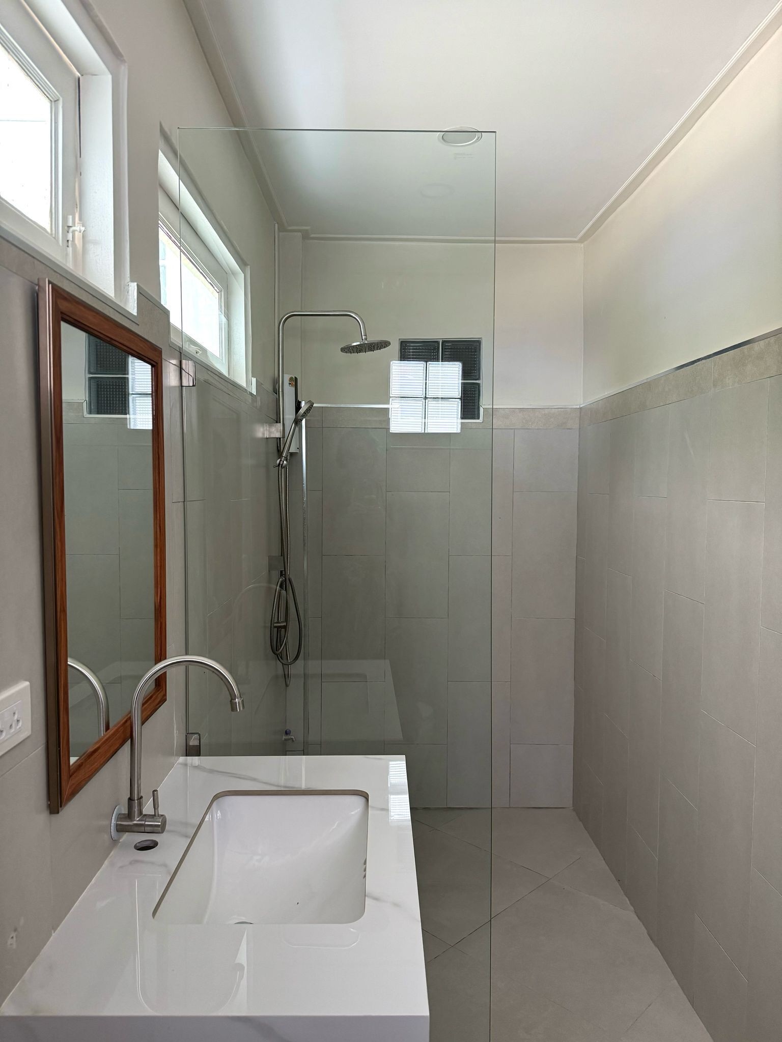 A modern bathroom with a glass-enclosed shower, a white sink, and a large mirror.