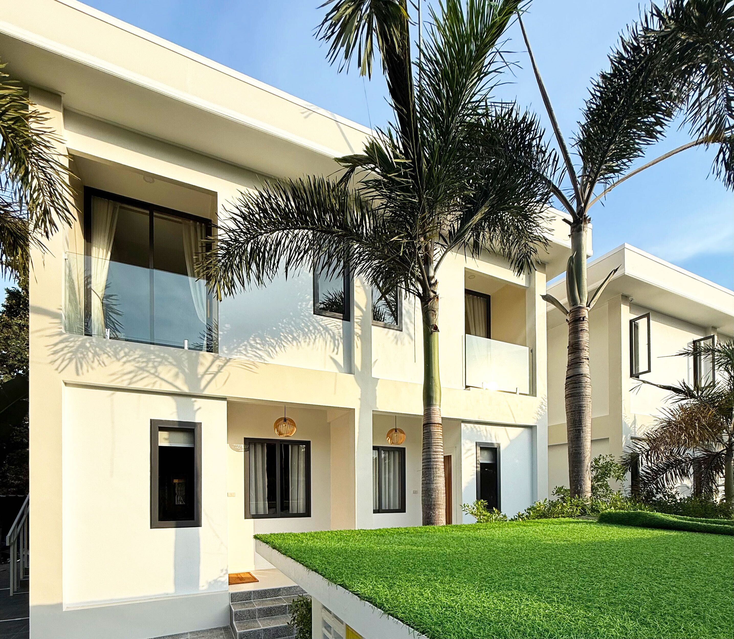 A modern building with a flat roof, large windows, and a well-maintained lawn with palm trees.