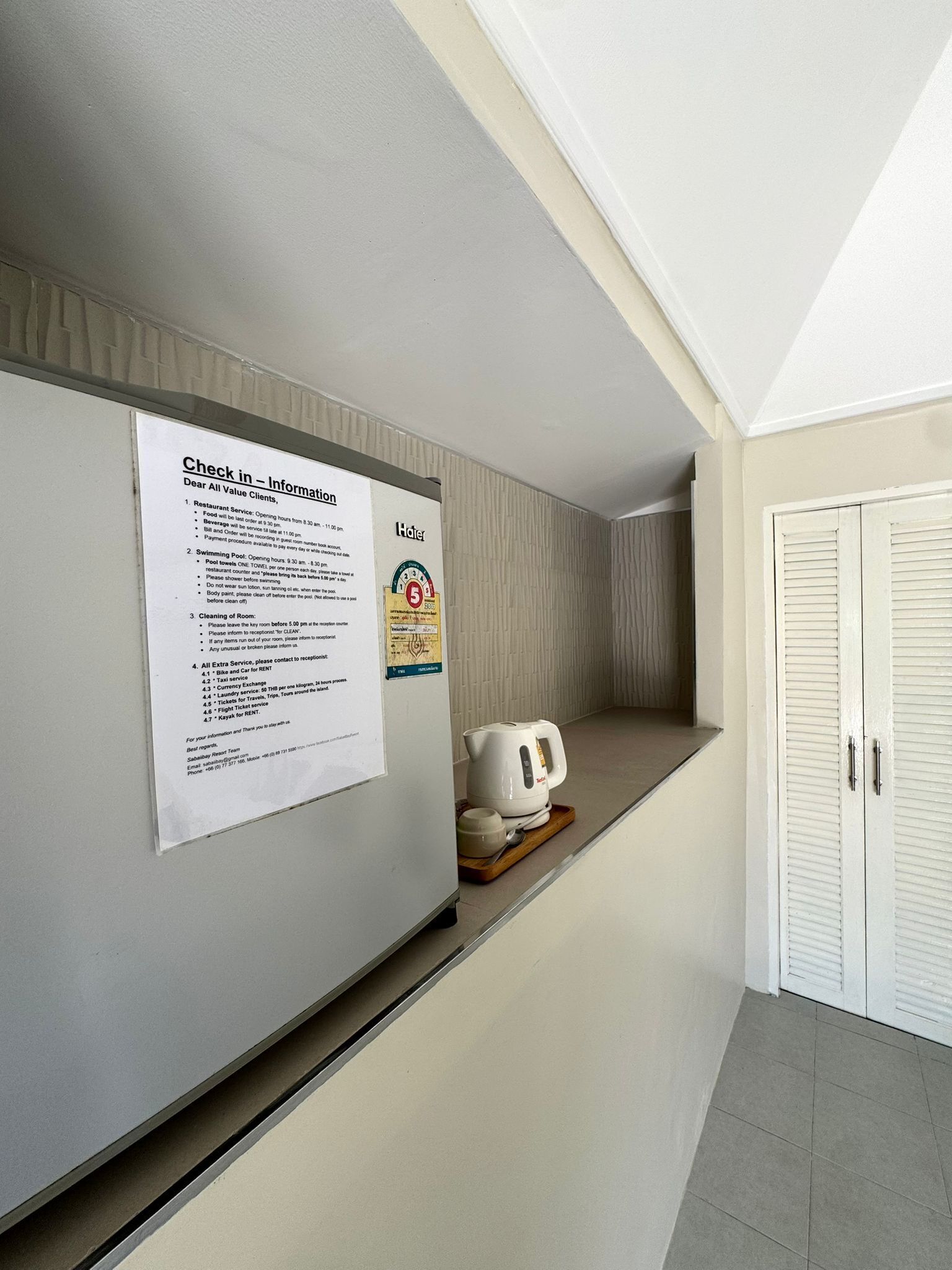 A hotel corridor with a notice board, a kettle, and a closed door.
