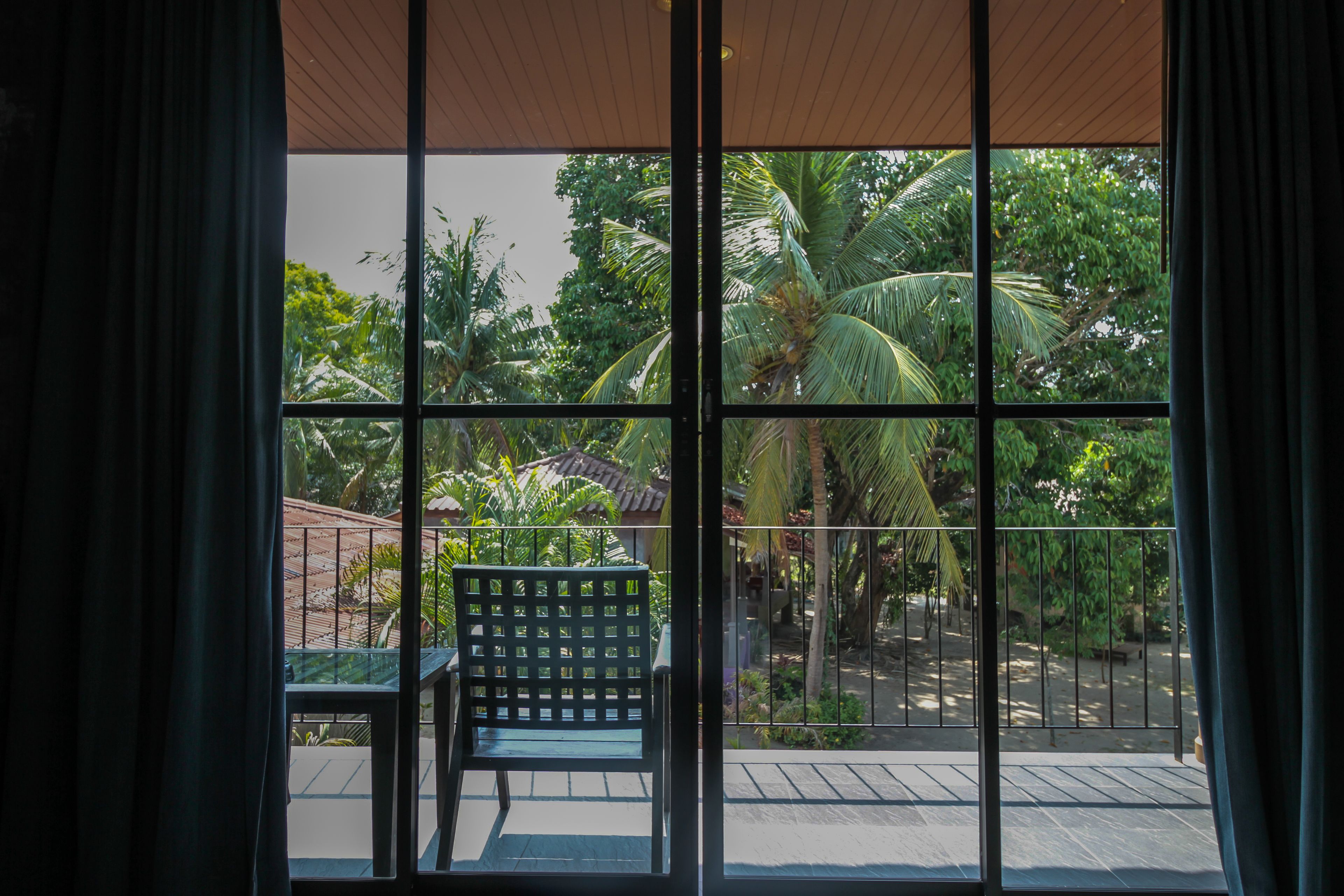 Ein Zimmer mit großem Fenster und Blick auf einen Garten mit Palmen und einer Holzterrasse.