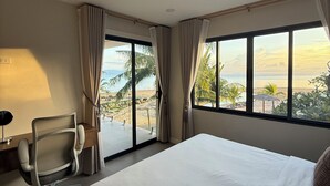 A hotel room with a large bed, a desk with a chair, and a view of the beach and palm trees through the windows. - Sabaii Bay Resort (Ko Pha-ngan)