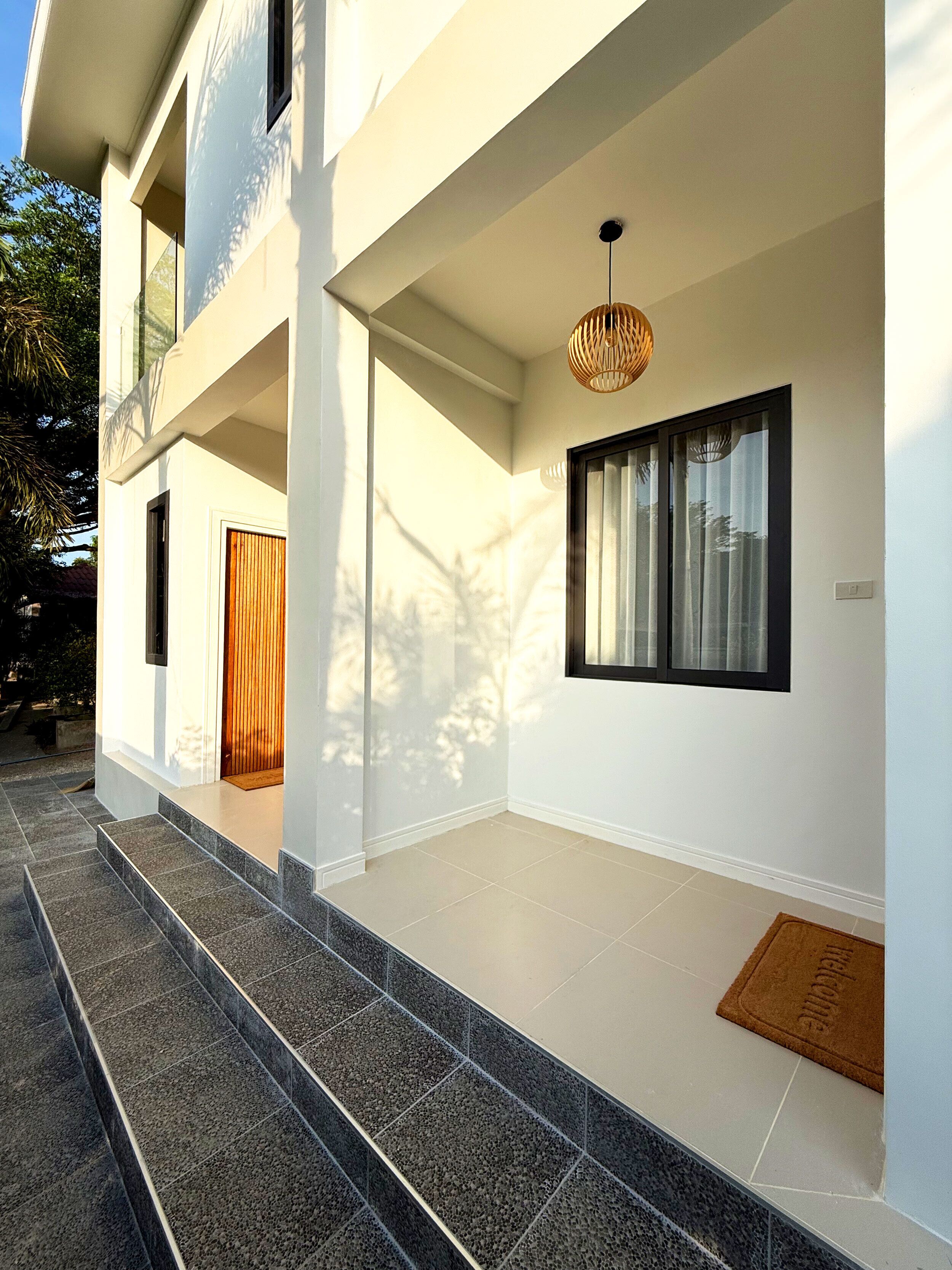 Un edificio moderno con una escalera que conduce a una entrada cubierta, un ventanal con cortinas y una lámpara colgante.