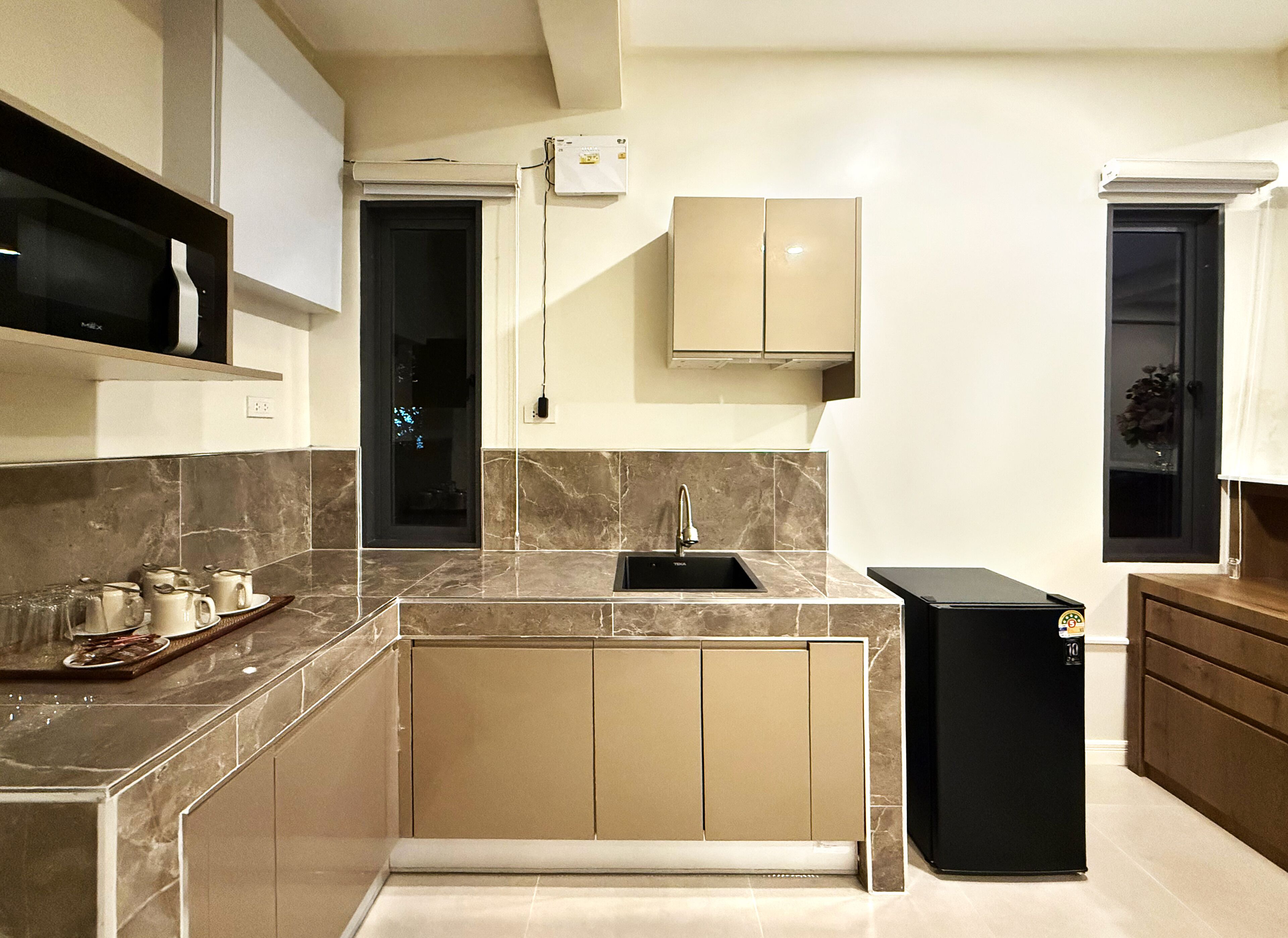 A modern kitchen with marble countertops, a black refrigerator, and built-in cabinets.