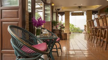 A restaurant with wicker chairs, a table with a vase of flowers, and a sign reading "Korbuah House".