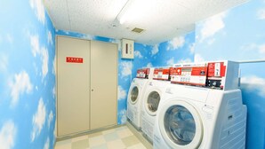A laundry room with three front-loading washing machines, a ceiling light, and a door with a sign in Japanese. - Shin Osaka Hotel (Osaka)