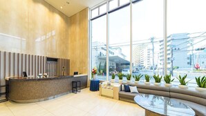 A modern reception area with a curved counter, seating, and large windows offering a city view. - Shin Osaka Hotel (Osaka)