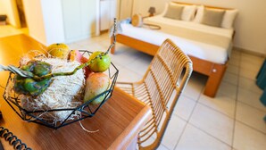 A cozy room with a bed, a dining table with a fruit basket, and a wicker chair. - Le Kervéguen (Saint-Paul)