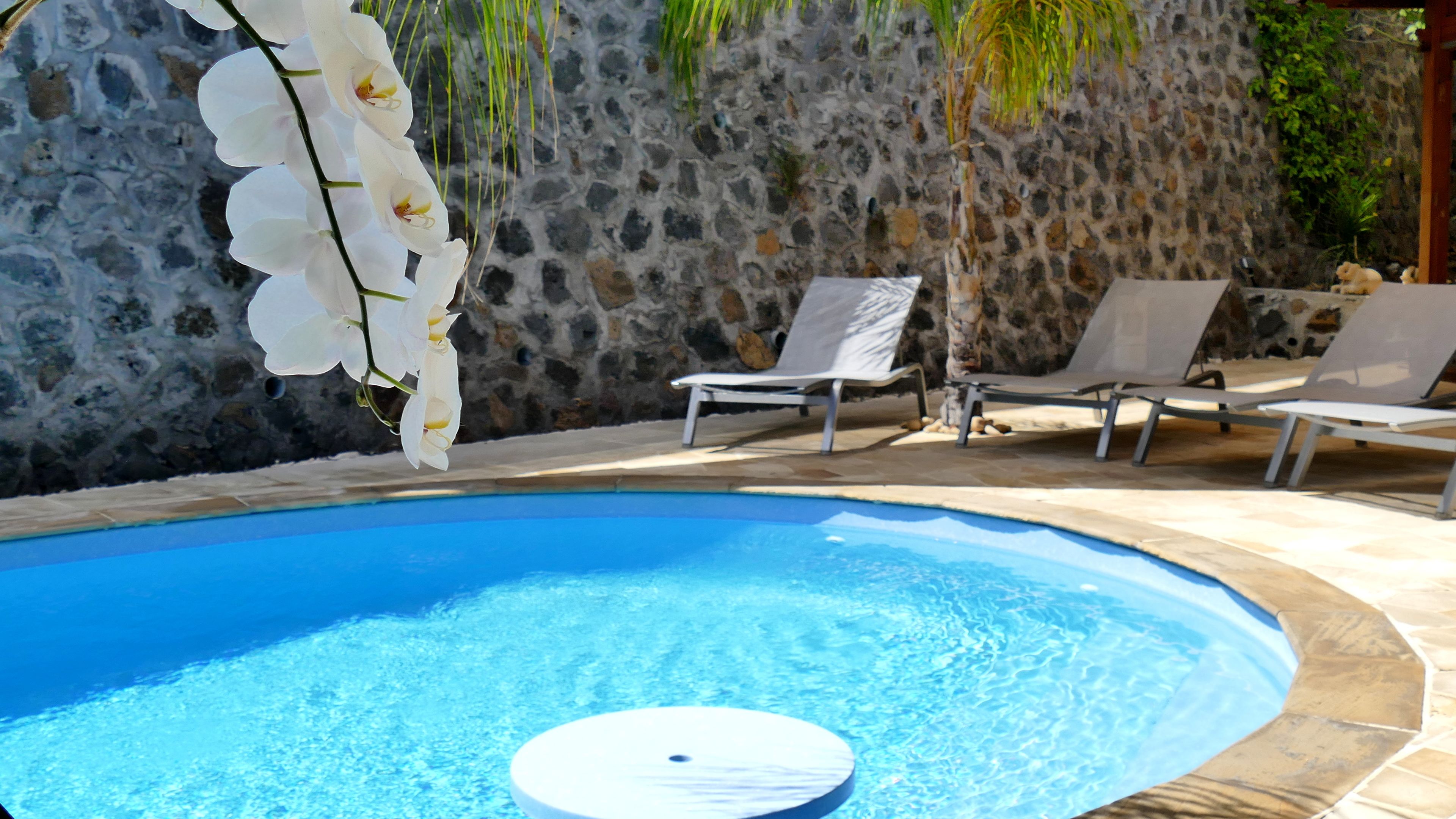 A swimming pool with a white floating platform, surrounded by lounge chairs and a stone wall.