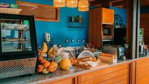 A breakfast bar with a display case, wicker hanging lights, and a variety of breakfast items including fruits, bread, and pastries. - Le Kervéguen (Saint-Paul)