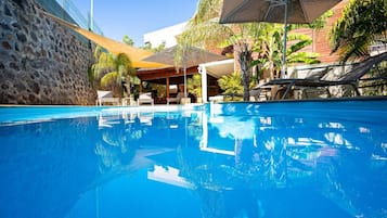 Una piscina al aire libre, sombrillas, sillones reclinables de piscina